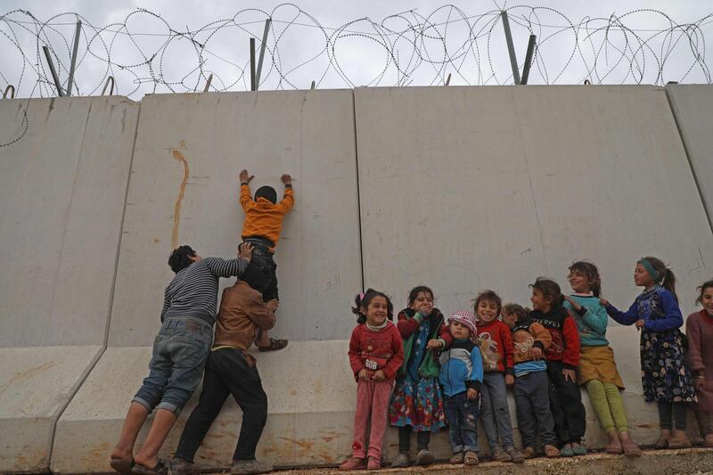 Displaced Syrian children try to climb over the Turkish border wall at an informal camp in Kafr Lusin village in Syria's northwestern province of Idlib.  AFP