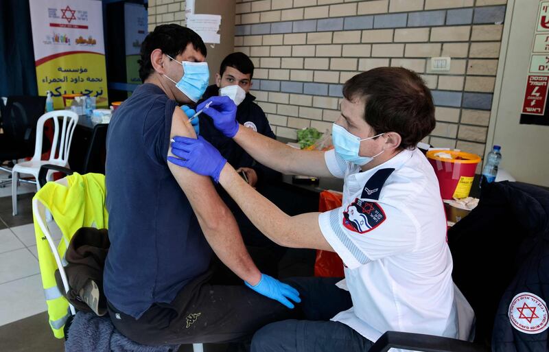 A paramedic with Israel's Magen David Adom medical services administers the Pfizer-BioNTech COVID-19 vaccine to a Palestinian man on February 23, 2021 at Qalandia checkpoint on the crossing between the West Bank city of Ramallah and Israeli-annexed east Jerusalem. / AFP / AHMAD GHARABLI
