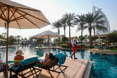Tourists sunbathe by the pool of Al Naseem hotel in Dubai, UAE on July 7, 2020, with a view of the iconic Burj Al Arab hotel in the background. Dubai reopened its doors to international visitors in the hope of reviving its tourism industry after a nearly four-month closure. AFP