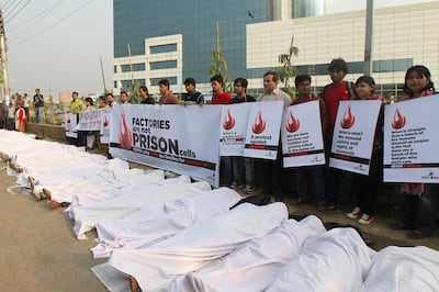 Bangladeshi activists pretend to be dead, wrapped in blankets,  following a deadly fire in a garment factory during a protest in Dhaka on November 29, 2012. Police arrested three managers of Tazreen Fashion factory hit by a fire, following charges that they stopped workers from leaving the burning plant when the fire alarm sounded, insisting that it was just a routine drill, referring to a weekend blaze at a local garment factory that left 110 people dead and more than 100 injured.  AFP PHOTO/STR (Photo by STR / AFP)