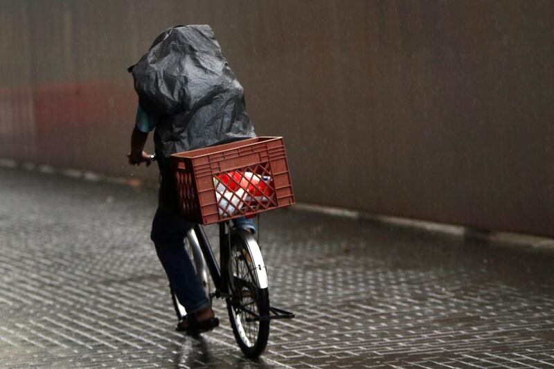 A cyclist shields himself from the rain in Abu Dhabi. Delores Johnson / The National