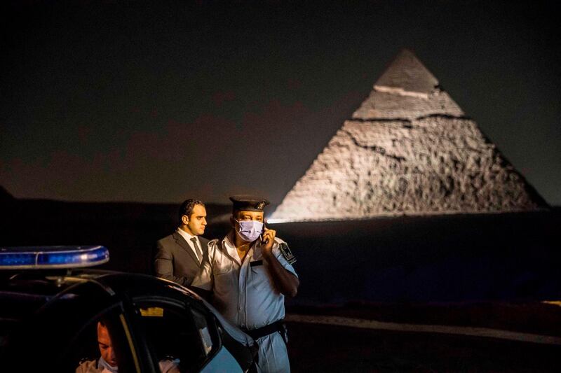 A policeman speaks on the phone while standing next to a police car at a promontory overlooking the Pyramid of Khafre (Chephren) at the Giza Pyramids necropolis on the southwestern outskirts of the Egyptian capital Cairo during an official ceremony launching the trial operations of the site's first environmentally-friendly electric bus (foreground) and restaurant as part of a wider development plan at the necropolis.   AFP