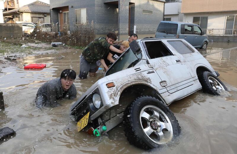 TOPSHOT - Residents try to upright a vehicle stuck in a flood hit area in Kurashiki, Okayama prefecture on July 9, 2018. Rescue workers, police and troops in Japan battled on July 9 to reach people feared trapped by devastating flooding and landslides after days of record rainfall killed at least 75 people. - Japan OUT
 / AFP / JIJI PRESS / JIJI PRESS
