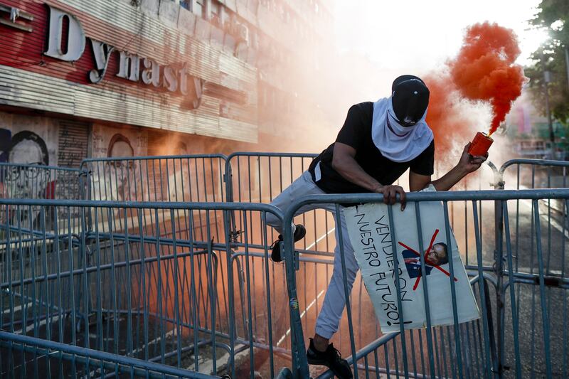 A protester scales barricades as he holds a smoke flare during a rally against copper mining, outside the National Assembly in Panama City, Panama. EPA