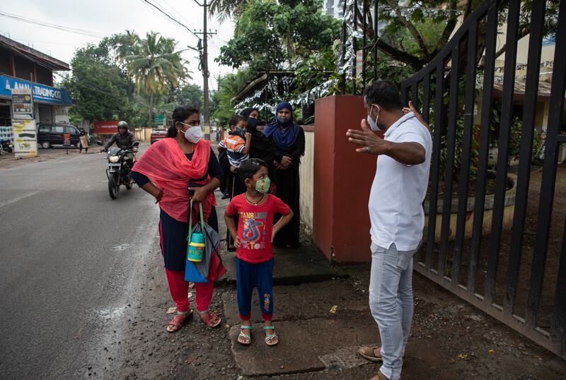 A school staff member gestures to parents waiting outside the gate to maintain social distancing.