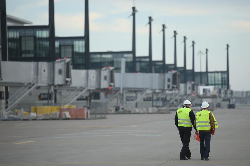 SCHOENEFELD, GERMANY - NOVEMBER 04:  Two workers stand on the tarmac next to the main arrivals and departures hall of the unfinished BER Willy Brandt Berlin Brandenburg International Airport on November 4, 2014 in Schoenefeld, Germany. According to media reports November 17, 2014, Brandenburg State Finance Minister Christian Goerke stated that an opening of the new airport is possible for 2017. The airport, originally scheduled to open in 2011, has been plagued by a massive design flaw in its fire safety system, cost overruns, delays and most recently a bribery scandal.  (Photo by Sean Gallup/Getty Images)