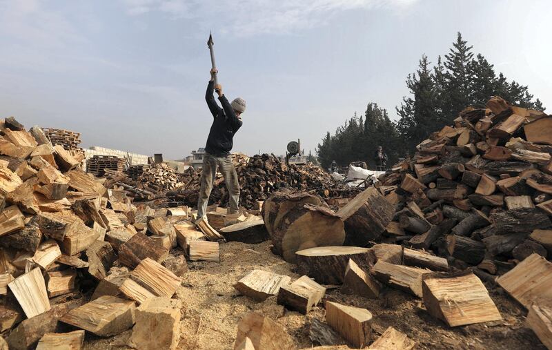 A displaced Syrian cuts wood logs out of tree trunks, destined to be sold to compatriots who fled conflict zones, to be used as a less expensive alternative to fuel for heating during the winter season, on the outskirts of the northwestern city of Idlib, on December 11, 2020. (Photo by OMAR HAJ KADOUR / AFP)