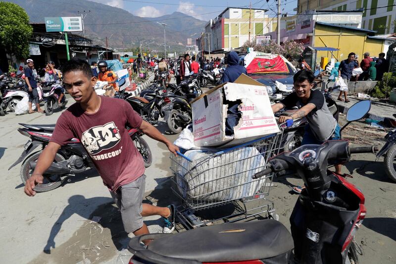Indonesian men drag a shopping trolley with goods looted from a shopping mall in Palu, Central Sulawesi, Indonesia.  EPA