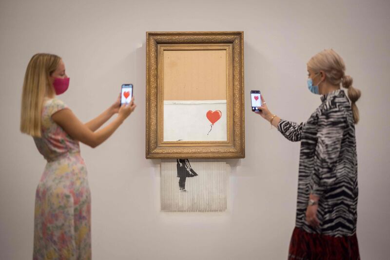 Assistants pose by an artwork titled 'Love is the Bin' by British street artist Banksy during a photocall at Sotheby’s auction house in central London. AFP