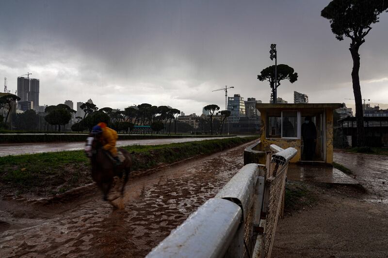 A jockey in full wet-weather gear spurs his horse past the trainers' huts.