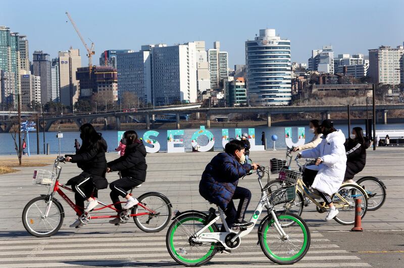 Young people wearing face masks ride bicycles at a park in Seoul. AP Photo