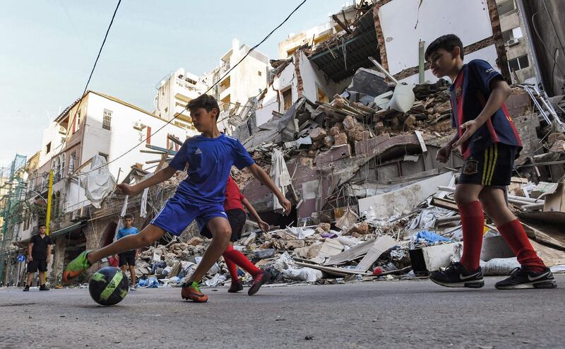 Children play with a football past rubble and destruction along a street in the Gemmayzeh district of Lebanon's capital Beirut in the aftermath of the monster blast at the nearby post which devastated the city.   AFP