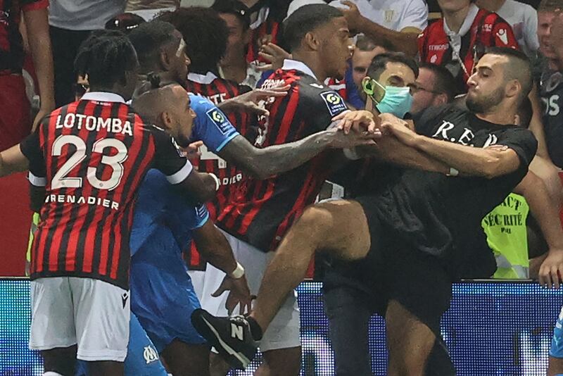 Marseille's French midfielder Dimitri Payet (2nd L) reacts as players from OGC Nice (red and black jersey) and Olympique de Marseille (blue jersey) stop a fan invading the pitch  during the French L1 football match between OGC Nice and Olympique de Marseille (OM) at the Allianz Riviera stadium in Nice, southern France on August 22, 2021.  - The French Ligue 1 game between Nice and Marseille was halted on August 22, 2021, when fans of the home side invaded the pitch and angrily confronted opposing player Dimitri Payet.  An AFP journalist at the game said trouble flared in the 75th minute when Marseille star Payet, who had been targeted by plastic bottles every time he took a corner, lobbed one back into the stands.  (Photo by Valery HACHE  /  AFP)