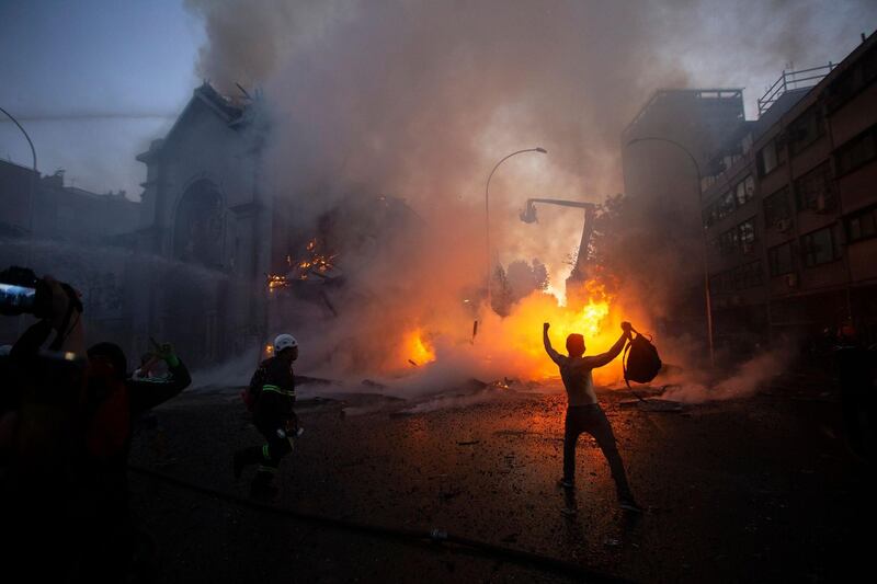 A demonstrator celebrates next to a firefighter after the dome of the church of Asuncion fell down burning in flames after being set on fire during a protest on the commemoration of the first anniversary of the social uprising in Chile, in Santiago as the country prepares for a landmark referendum.  AFP