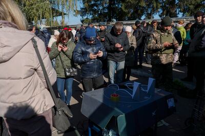 Ukrainian civilians and soldiers checking their mobile phones while standing next to an internet booster station, in the recently recaptured city of Kupiansk, east of Kharkiv. EPA