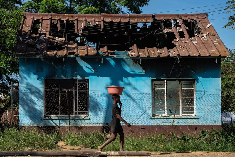 A young woman carries a bowl on her head as she walks past the shell of the burnt-out offices belonging to the ruling ZANU PF party's Kadoma district in  Kadoma, Zimbabwe. AFP