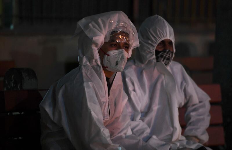 TOPSHOT - Relatives in personal protective equipment (PPE) suits watch the cremation of their loved one who died of the Covid-19 coronavirus at Nigambodh Ghat Crematorium in New Delhi on April 28, 2021. / AFP / TAUSEEF MUSTAFA
