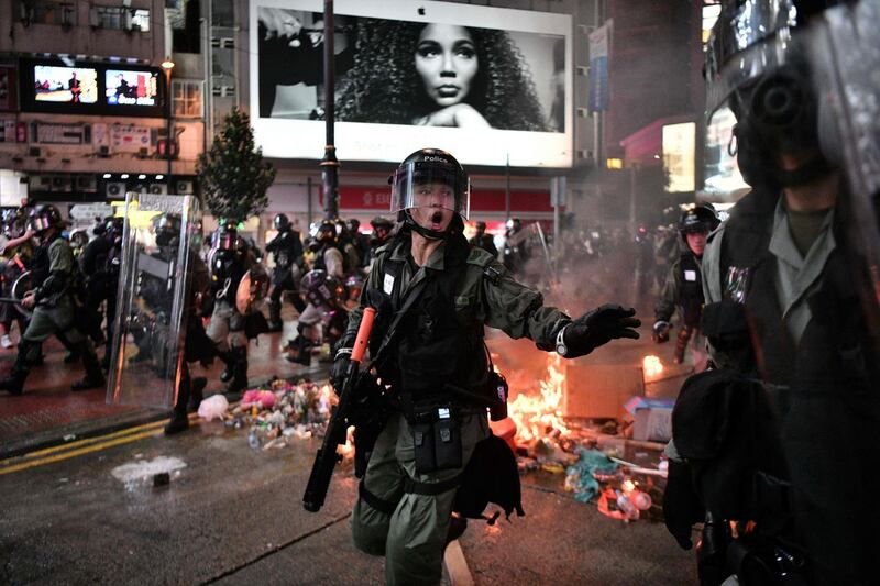 Police run past debris set alight by protesters in the Causeway Bay area of Hong Kong.   AFP