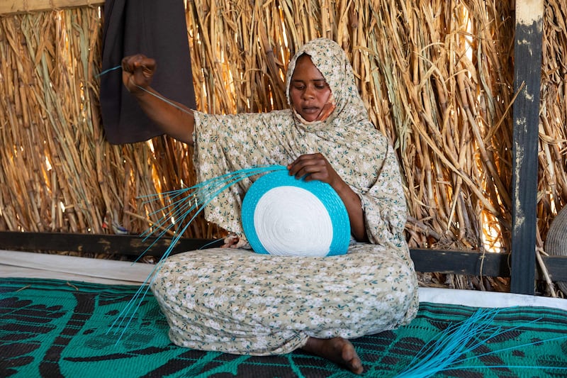 Twenty-three-year-old Sudanese refugee and student Asha Mohamat Mousa weaves a dish with plastic threads inside her shelter in the Tongori refugee camp