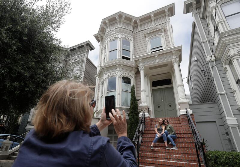 Aries Layton, seated left, and her aunt Kelsy Layton pose as Debra Layton, Aries' grandmother and Kelsy's mother, foreground, takes photos outside a Victorian home made famous by the television show "Full House" in San Francisco, Tuesday, July 17, 2018. Tour buses will no longer be swinging by the San Francisco house made famous in the popular 1990s sitcom "Full House." The San Francisco Municipal Transportation Agency voted Tuesday to ban commercial vehicles from Broderick Street after neighbors complained.  (AP Photo/Jeff Chiu)