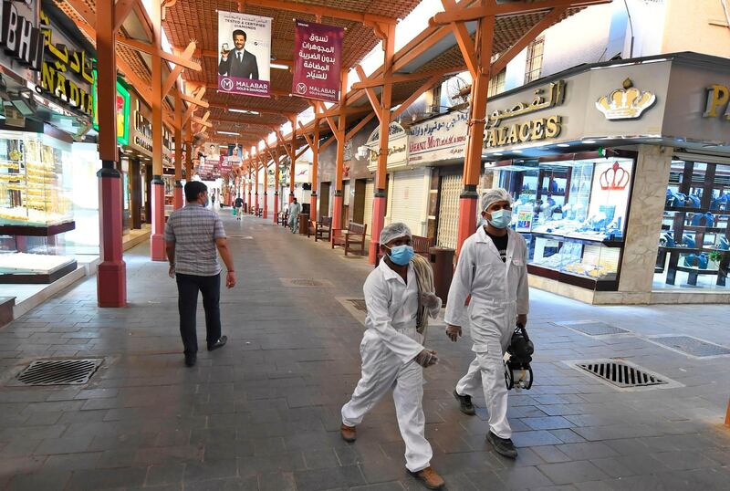 Workers dressed in protective clothing and masks walk with sterilisation gear due to the COVID-19 coronavirus pandemic past jewellers' shops at the Dubai Gold Souk in the Gulf emirate on May 12, 2020, as markets re-open amidst an easing of pandemic restrictions.  / AFP / Karim SAHIB
