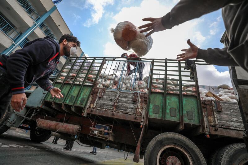 Palestinian workers at the United Nation Relief and Works Agency (UNRWA) wearing protective masks upload food aid rations for poor refugee families, at a UN school in Gaza City.  EPA