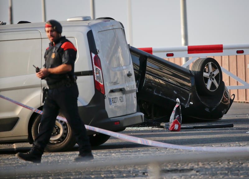 A police officer walks near an overturned car at the spot where terrorists were intercepted by police in Cambrils, Spain, Friday, Aug. 18, 2017. The police force for Spain's Catalonia region says the five suspects shot and killed in the resort town of Cambrils were carrying bomb belts, which have been detonated by the force's bomb squad. (AP Photo/Emilio Morenatti)