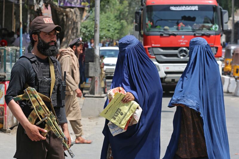 Burqa-clad women walk past a Taliban security guard along a street in Jalalabad in Afghanistan. AFP