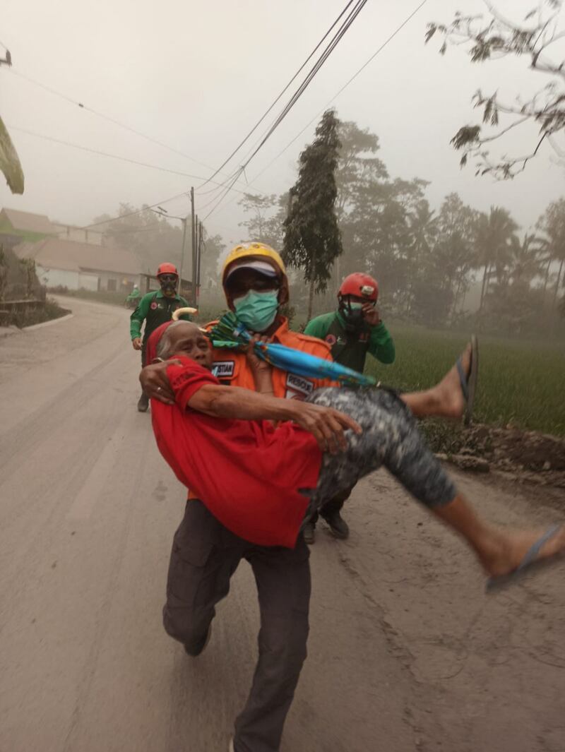 A rescuer helps an elderly resident following the eruption of Mount Semeru. Reuters