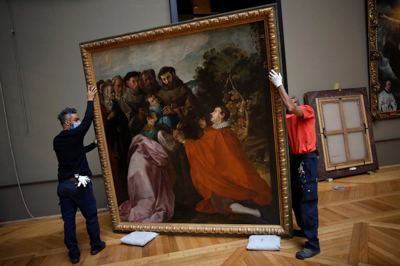 Workers handle the painting 'The Healing of Saint Bonaventure as a Child by Saint Francis' by Spanish painter Francisco de Herrera in the Louvre on February 9, 2021. AP