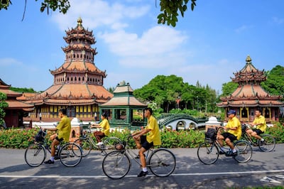 Schoolchildren ride bicycles past a replica of the Phra Kaew Pavilion in the Ancient City Heritage Park in Samut Prakan, some 25km south of Bangkok on December 9, 2020. / AFP / Mladen ANTONOV
