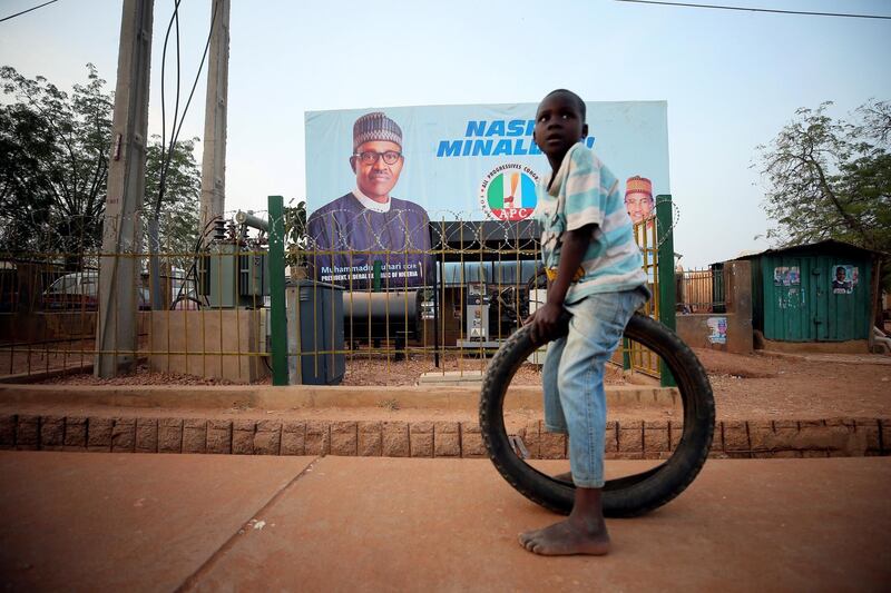 A boy sits on a tyre in front of a billboard on the eve of Nigeria's 2019 presidential election in Daura, Katsina State, Nigeria. Reuters