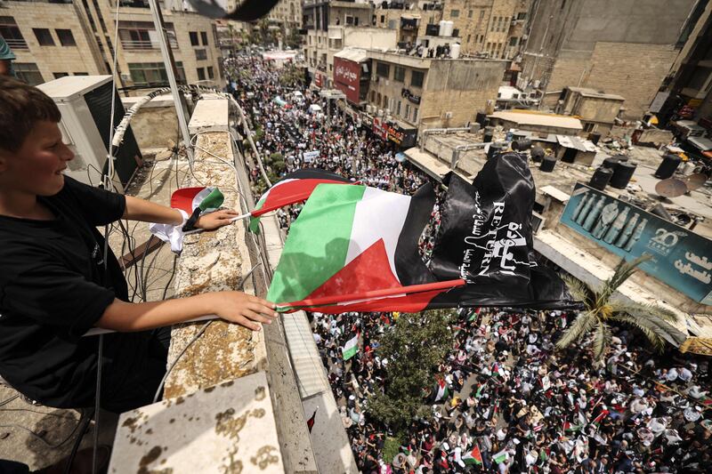 A young Palestinian waves national flags from a rooftop as people march in a rally marking the 74th anniversary of the Nakba (catastrophe) in the occupied West Bank town of Ramallah. AFP