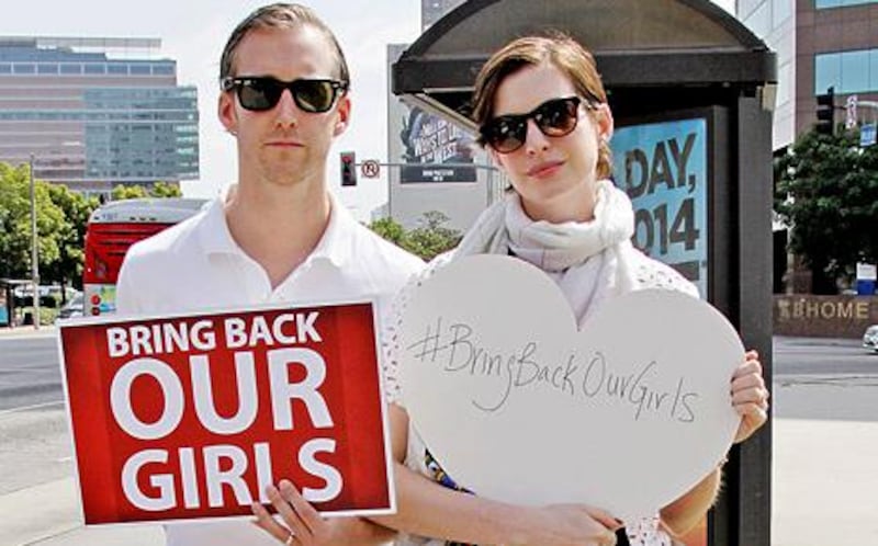 Adam Schulman and his wife Anne Hathaway hold up signs showing their support for the Bring Back Our Girls campaign. Courtesy Anne Hathaway
