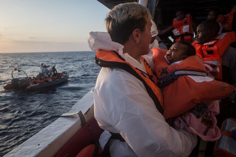 LAMPEDUSA, ITALY - JUNE 10: A crewmember from the Migrant Offshore Aid Station (MOAS) Phoenix vessel holds a child as they wait to transfer refugees and migrants to a waiting Italian coastguard ship after being rescued at sea earlier in the day on June 10, 2017 off Lampedusa, Italy. An estimated 230,000 refugees and migrants will arrive in Italy this year as numbers of refugees and migrants attempting the dangerous central mediterranean crossing from Libya to Italy continues to rise since the same time last year. So far this year more than 58,000 people have arrived in Italy and 1,569 people have died attempting the crossing. Libya continues to be the primary departure point for refugees and migrants taking the central mediterranean route to Sicily. In an attempt to slow the flow of migrants, Italy recently signed a deal with Libya, Chad and Niger outlining a plan to increase border controls and add new reception centers in the African nations, which are key transit points for migrants heading to Italy. MOAS is a Malta based NGO dedicated to providing professional search-and-rescue assistance to refugees and migrants in distress at sea. Since the start of the year MOAS have rescued and assisted more than 4000 people and are currently patrolling and running rescue operations in international waters off the coast of Libya.  (Photo by Chris McGrath/Getty Images)