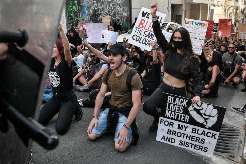 Youths kneel with placards reading 'Black Lives Matter' in front of riot police officers blocking the way in Athens during a rally against racism and police brutality and in support to the protests in US. AFP