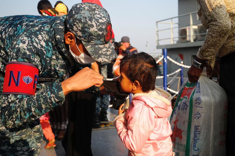 A Bangladesh navy personnel helps a child to wear a mask due to ongoing coronavirus disease (COVID-19) before getting on board a ship to move to Bhasan Char island in Chattogram, Bangladesh. Reuters