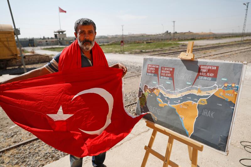 A man holds a Turkish flag as he stands next to a map showing Turkey's suggested operation in Syria, at the border between Turkey and Syria, in Akcakale, Sanliurfa province, southeastern Turkey. AP Photo