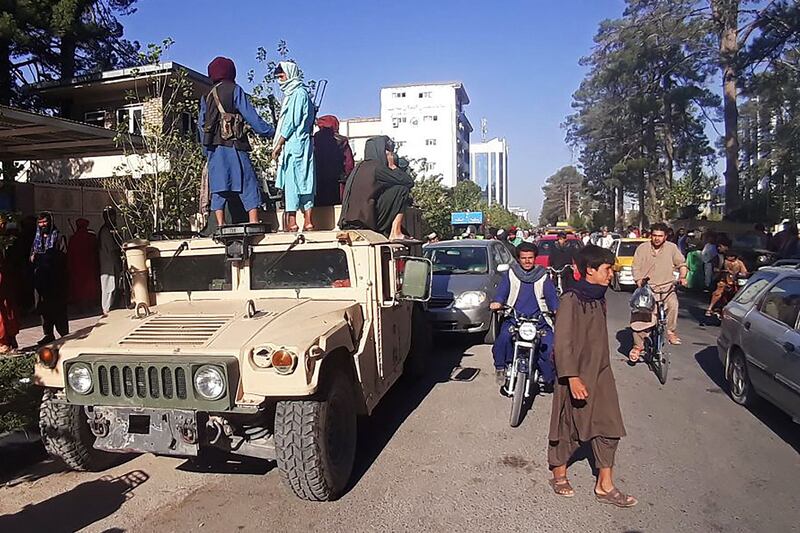 Taliban fighters stand on an abandoned military vehicle in Herat, on the same day insurgents also took Kandahar, Afghanistan's second-biggest city.