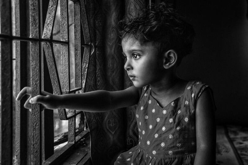 'Sadness' by Emran from Chittagong, Bangladesh. The description reads: 'With a pile of sadness in her eyes, she's sitting beside the window and waiting for the end of this lockdown so that she could go out and play with her friends'