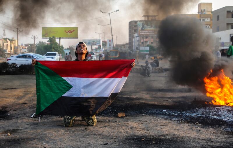 A Sudanese protester holds the national flag next to burning tyres during a demonstration in Khartoum.   EPA