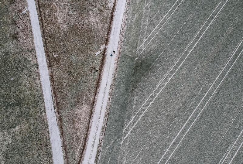 Two hikers walk between fields, covered with a soft blanket of snow, on the outskirts of Anspach, Germany. dpa via AP