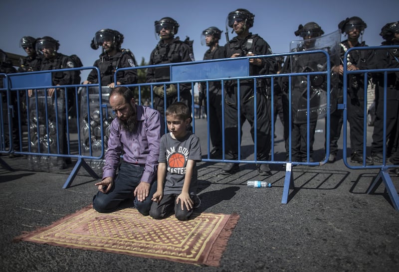 A Palestinian father and son pray under the gaze of Israeli police in East Jerusalem. Photo: Oliver Weiken / EPA