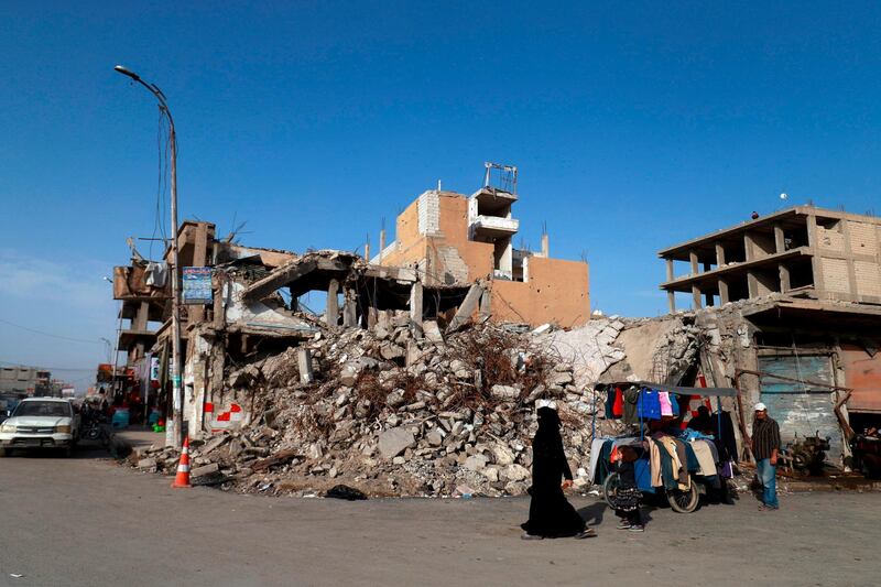 A woman walks past a street vendor and a destroyed building in the Syrian city of Raqa on October 18, 2018. A year after a US-backed alliance of Syrian fighters drove the Islamic State group from the northern city of Raqa, traumatised civilians still live in fear of near-daily bombings. / AFP / Delil souleiman
