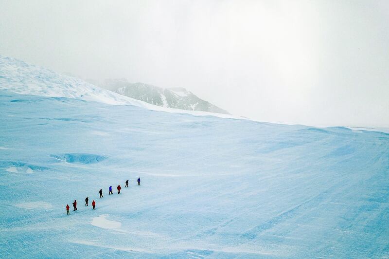 A group of guests hike up blue-ice during an excursion to the Drake Icefall on an overcast day.