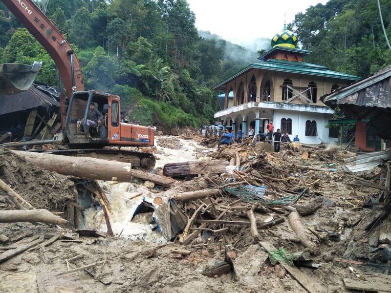 People use a heavy equipment to remove debris after flash floods hit the Saladi village in Mandailing Natal, North Sumatra on October 13, 2018. At least 10 people are dead when heavy rain led to flash floods and landslide in Indonesia, an official said on October 13. / AFP / AGUS SALIM
