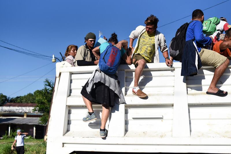 Honduran migrants heading in a caravan to the US, climb on a truck in Huixtla on their way to Mapastepec Chiapas state, Mexico, on October 24, 2018.

 Thousands of mainly Honduran migrants heading to the United States, a caravan President Donald Trump has called an "assault on our country", continued their march to the US after one-day rest in Huixtla, Chiapas state in Mexico. / AFP / Johan ORDONEZ 
