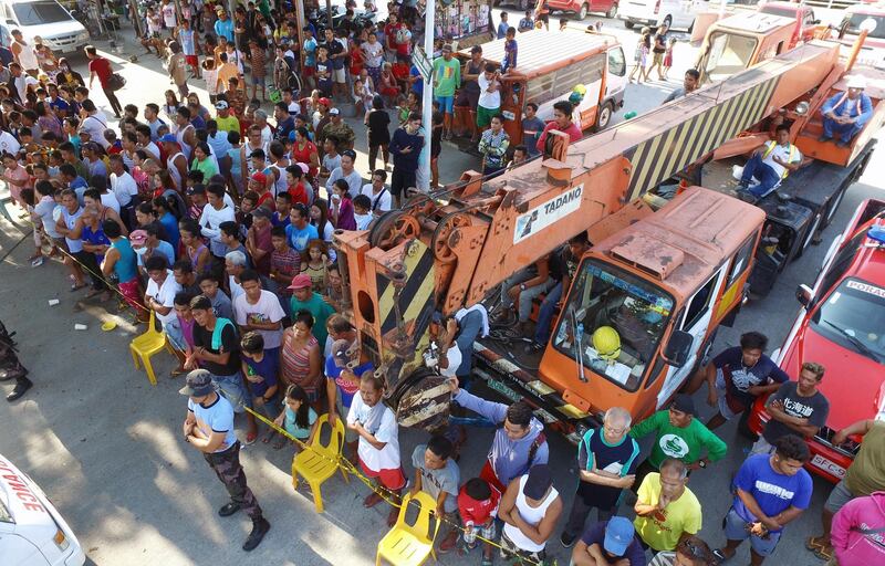 Residents look on as search operations continue at a collapsed commercial building in Porac town.