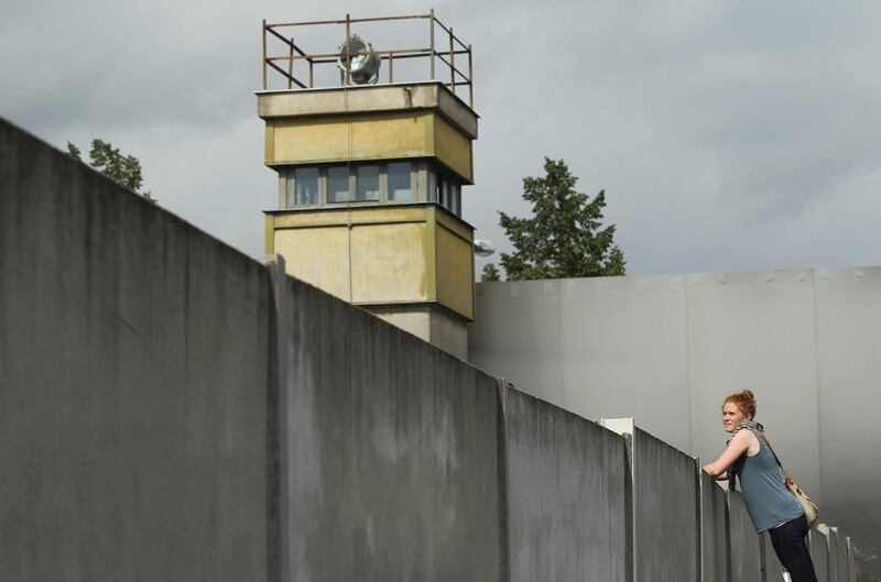 BERLIN, GERMANY - AUGUST 05:  A visitor standing on a ladder looks over a still-existing section of the Berlin Wall into the so-called 'death strip,' where East German border guards had the order to shoot anyone attempting to flee into West Berlin, as an original watchtower stands behind at the Bernauer Strasse memorial on August 5, 2011 in Berlin, Germany. The city of Berlin will mark the 50th anniversary of the construction of the Wall on August 13. The Berlin Wall was originally built in 1961 by the communist authorities of East Germany in order to stop East Germans from fleeing west, and up to an estimated 245 people died trying to do so until the Wall came down in 1989.   (Photo by Sean Gallup/Getty Images) *** Local Caption ***  120369697.jpg
