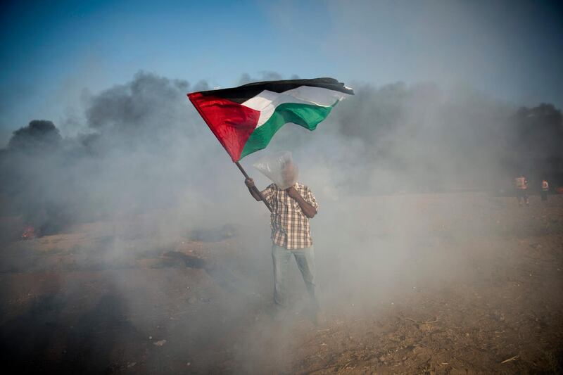 A Palestinian protester wears a plastic bag on his head as a protection from teargas as he waves a national flag during a protest at the Gaza Strip's border with Israel. AP